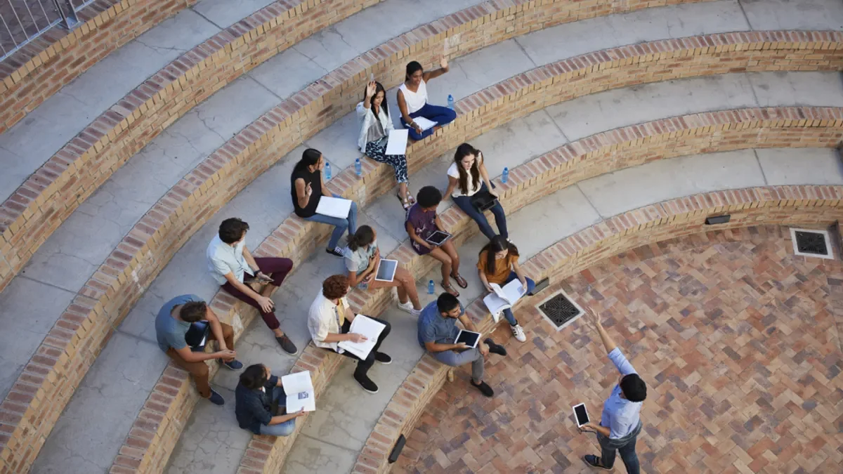 Students having class with book and tablets, in outside auditorium.